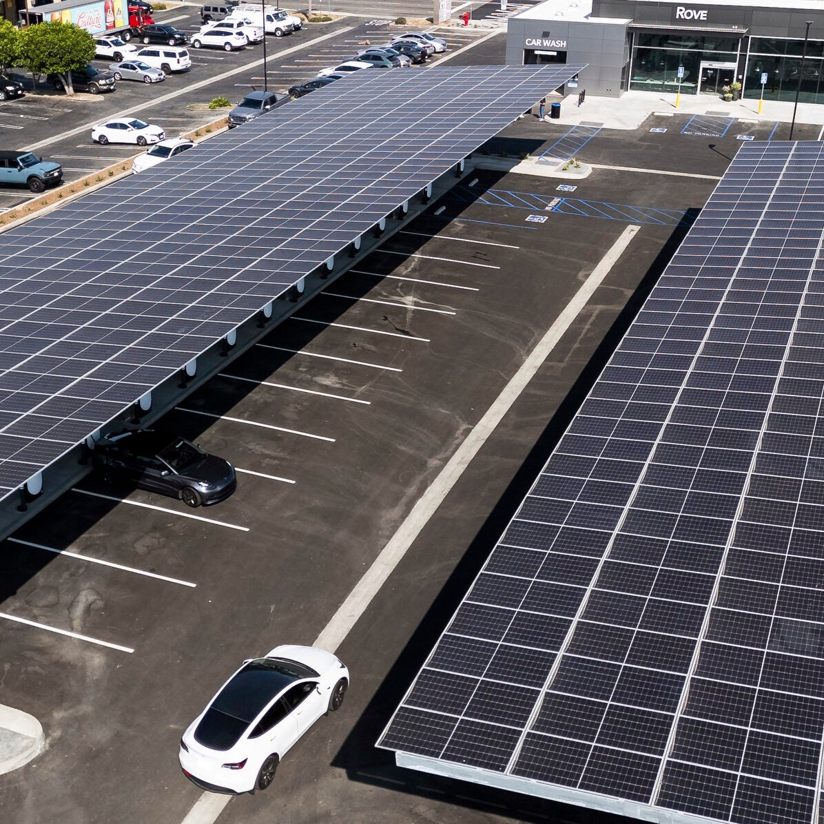Solar panels cover long rows of charging stations in the parking lot of a convenience store.