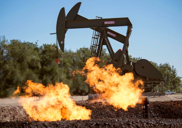 Flames rise out of low pipes in the ground as two jack pumps work in the background under a blue sky