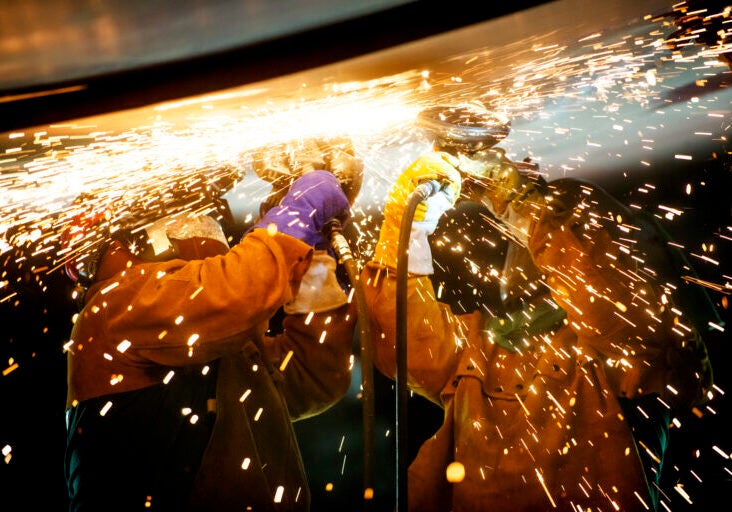 Two workers working overhead with sparks flying around them.