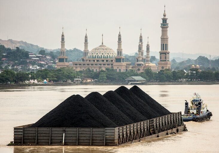 A tug pulls a coal barge past the Samarinda Islamic Center Mosque in East Kalimantan, Indonesia.