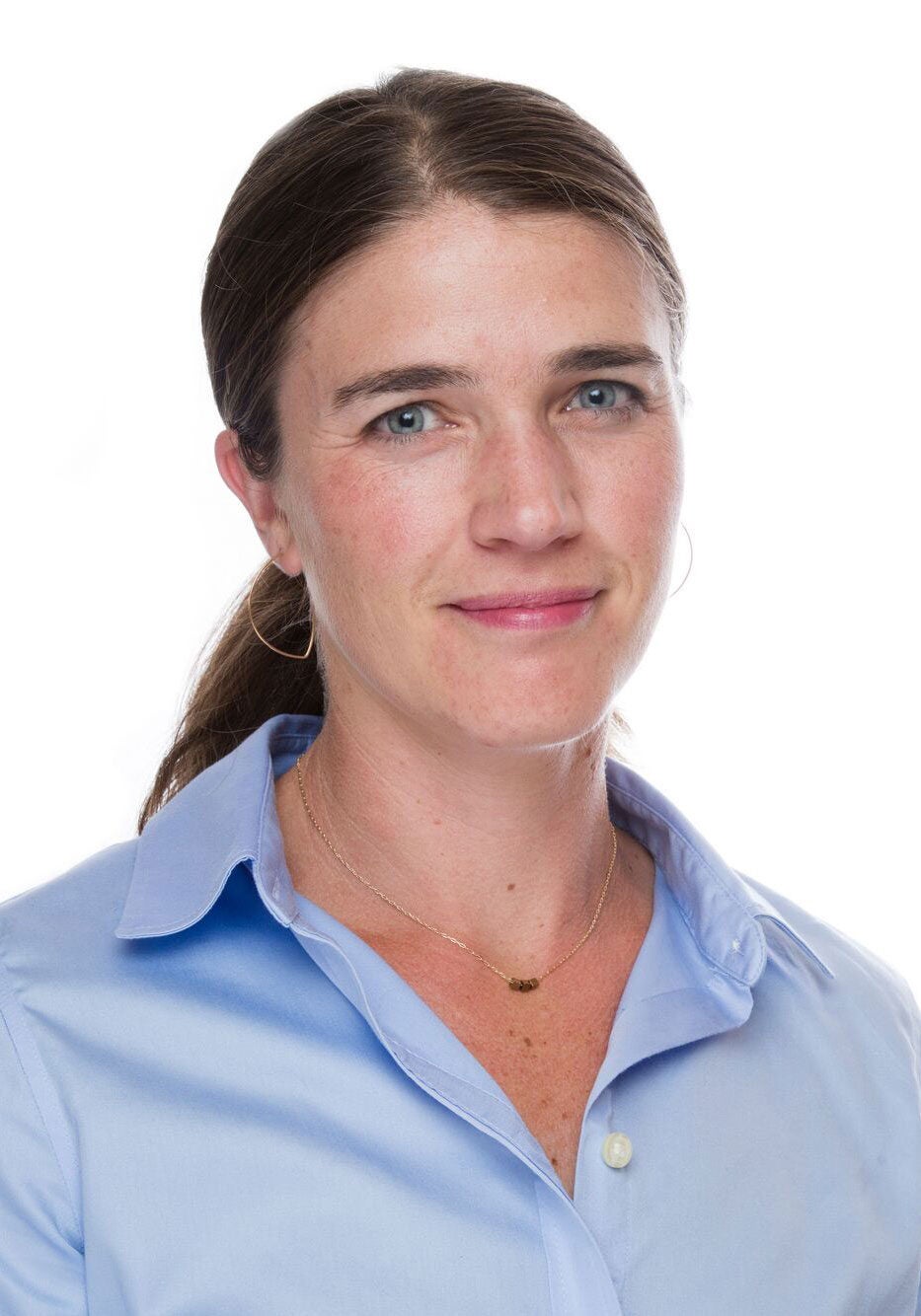 Jenny looks directly at the viewer with a slight smile. She's wearing a light blue collared button-down shirt. She's standing in front of a white backdrop.