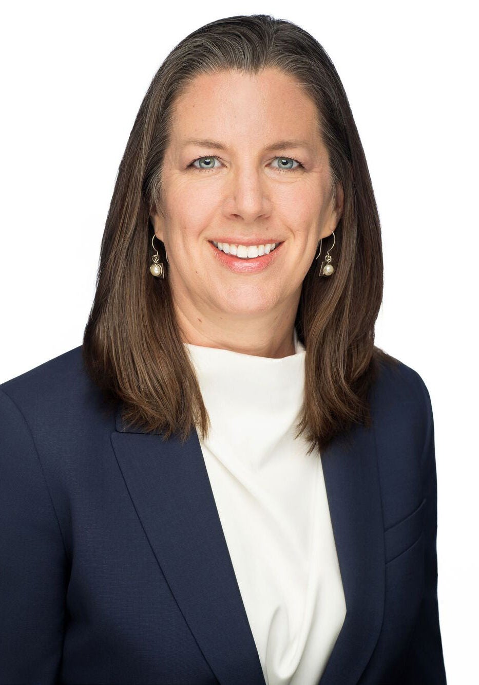 Laura looks directly at the viewer with a friendly, open smile. She is wearing a dark blue suit jacket and a white blouse. She is standing in front of a white backdrop.