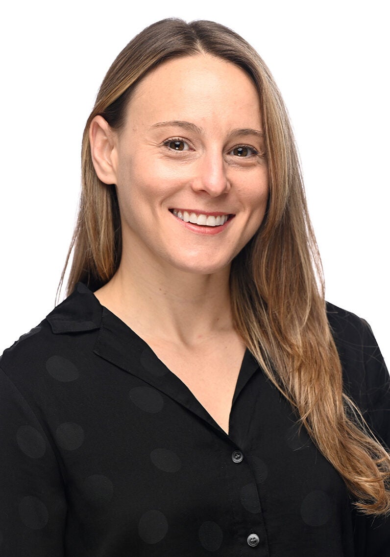 Lauren looks directly at the viewer with a friendly open smile. She's wearing a black blouse and in front of a white background.