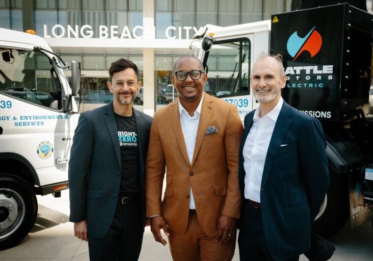 Mayor Rex Richardson and advocates stand alongside two electric garbage trucks.