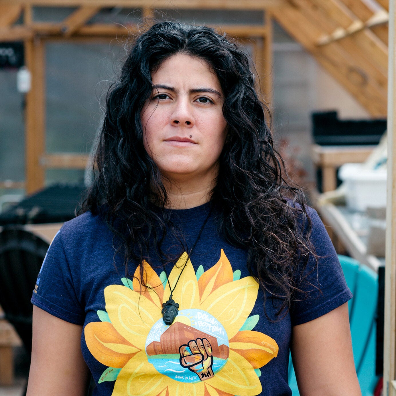 A woman looks directly at the camera with a serious expression standing in the door of a greenhouse.