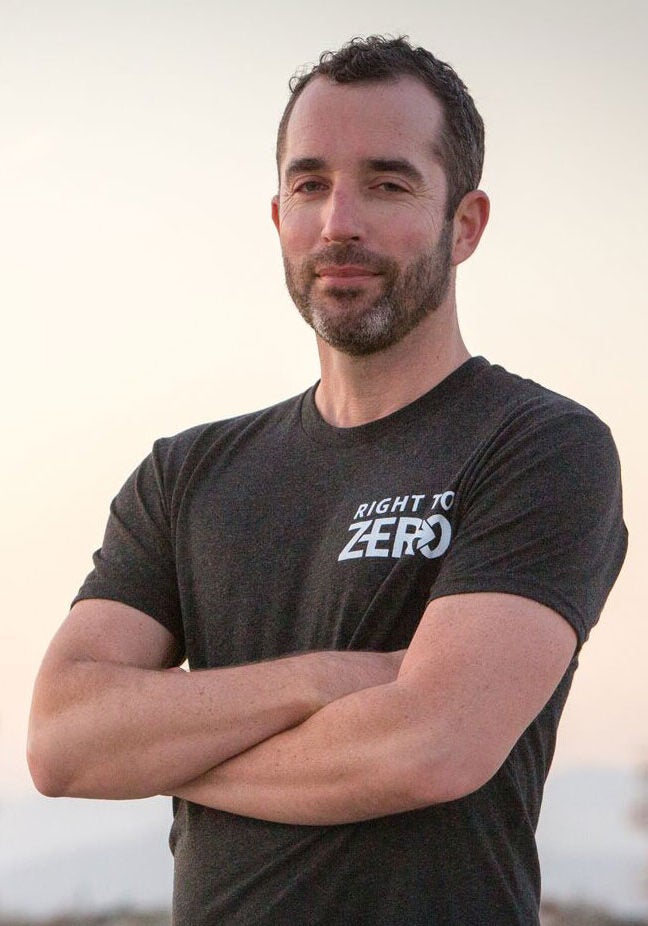 Matt stands facing the viewer, with his arms folded resolutely in front of him. He's wearing a black t-shirt with the text "Right to Zero" printed in the top left of the front. The background is blurred with light yellow and gray colors.