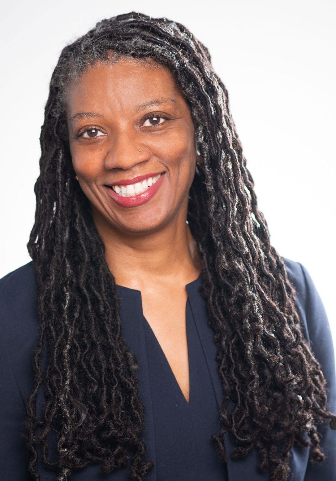 Melanie looks directly at the viewer with a friendly, open smile. She's wearing a dark blue business attire top and stands in front of a white backdrop.