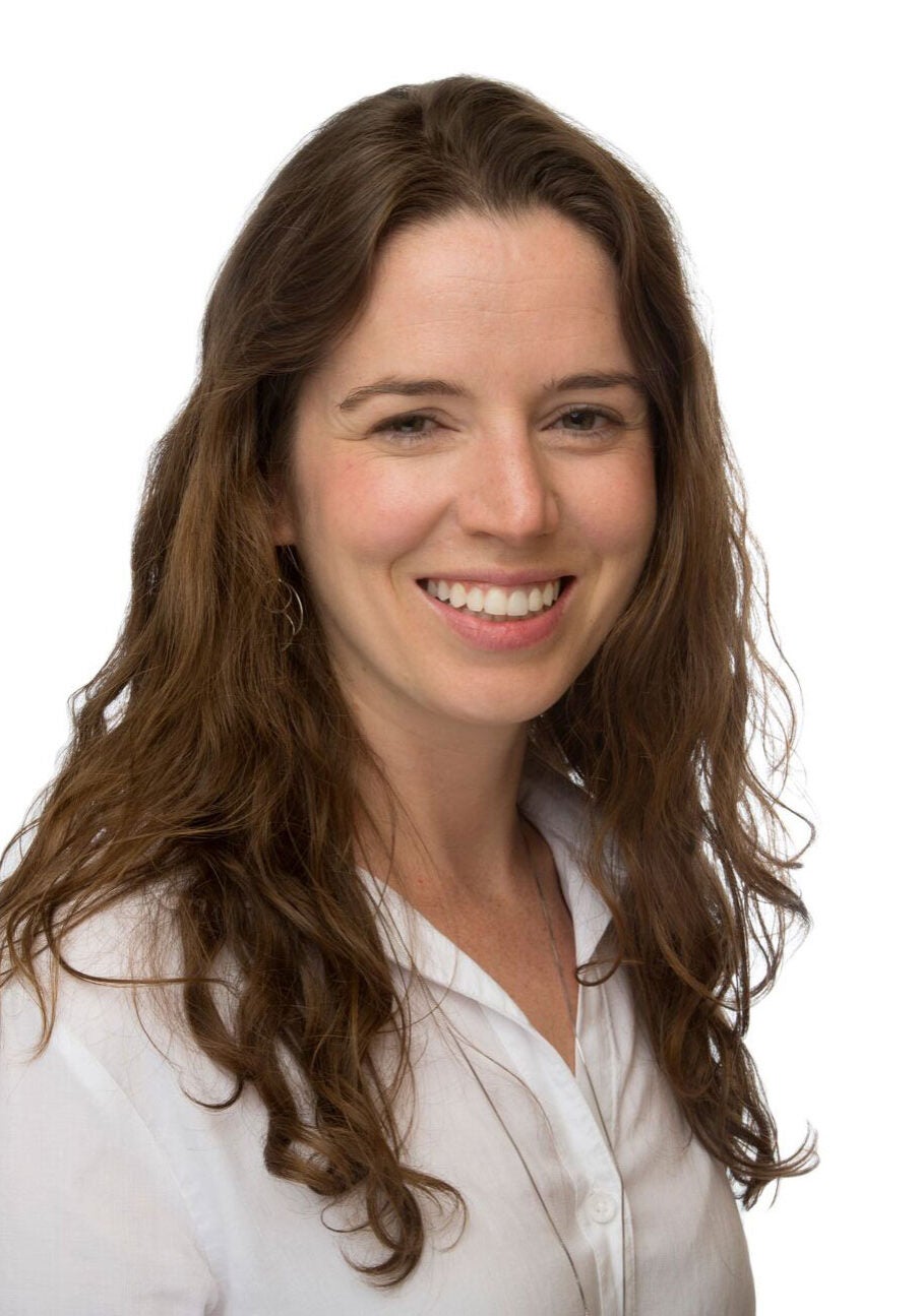 Moneen looks directly at the viewer with an open friendly smile. She's wearing a white, collared, buttoned down blouse, and stands in front of a white backdrop.