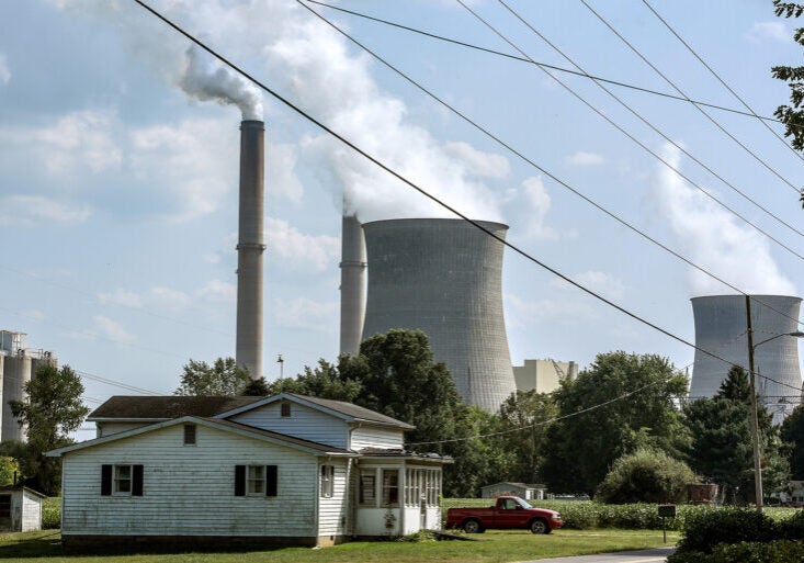 A farm house in the foreground with a large coal plant looming behind it.