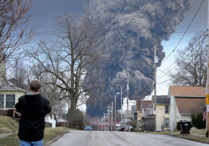 A man takes photos as a black plume rises over East Palestine, Ohio, as a result of a controlled detonation of a portion of the derailed Norfolk Southern train, Feb. 6, 2023. After toxic chemicals were released into the air from a wrecked train in Ohio, evacuated residents remain in the dark about what toxic substances are lingering in their vacated neighborhoods while they await approval to return home.