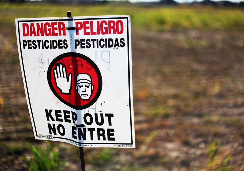A sign warns of pesticide application in a farm field.