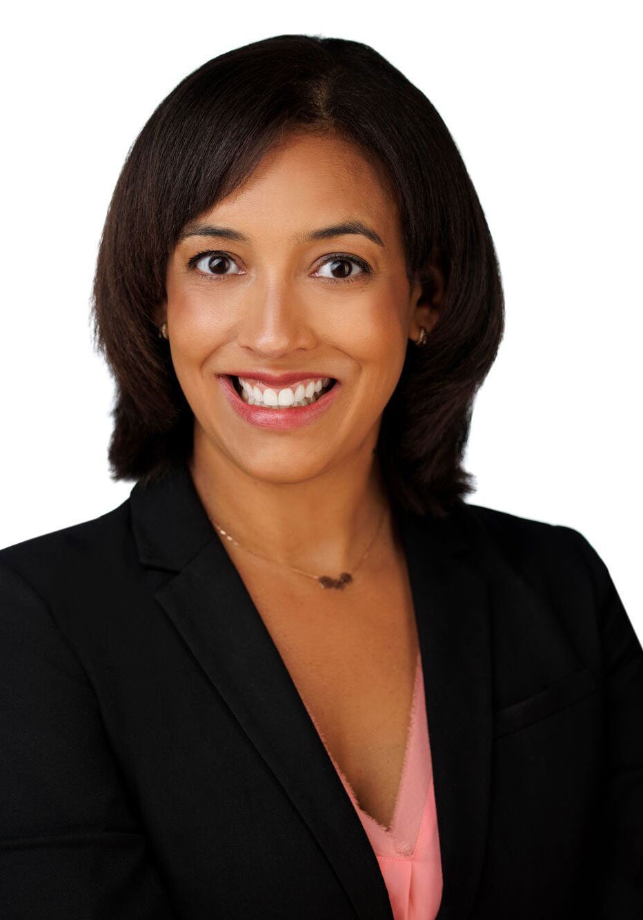 Rachel looks directly at the viewer with an open smile and bright eyes. She's wearing a black suit jacket and a coral-colored blouse. She's standing in front of a white backdrop.