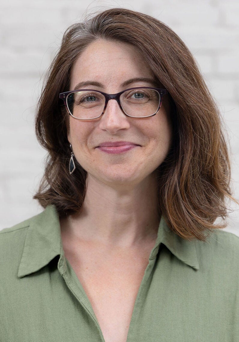 Rachel looks directly at the viewer with a friendly smile. She's wearing a light green collared shirt and standing in front of a light colored wall.