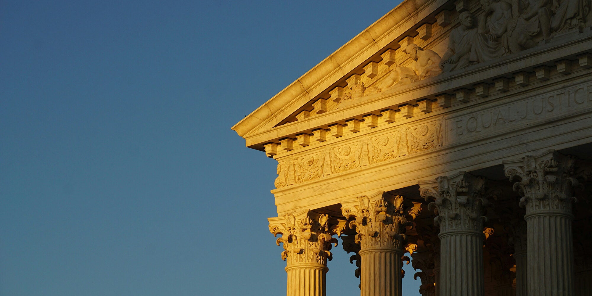 An exterior corner of the U.S. Supreme Court building's front face against a blue sky, bathed in golden sunlight fading into shadow with the words "Equal Justice" visible.