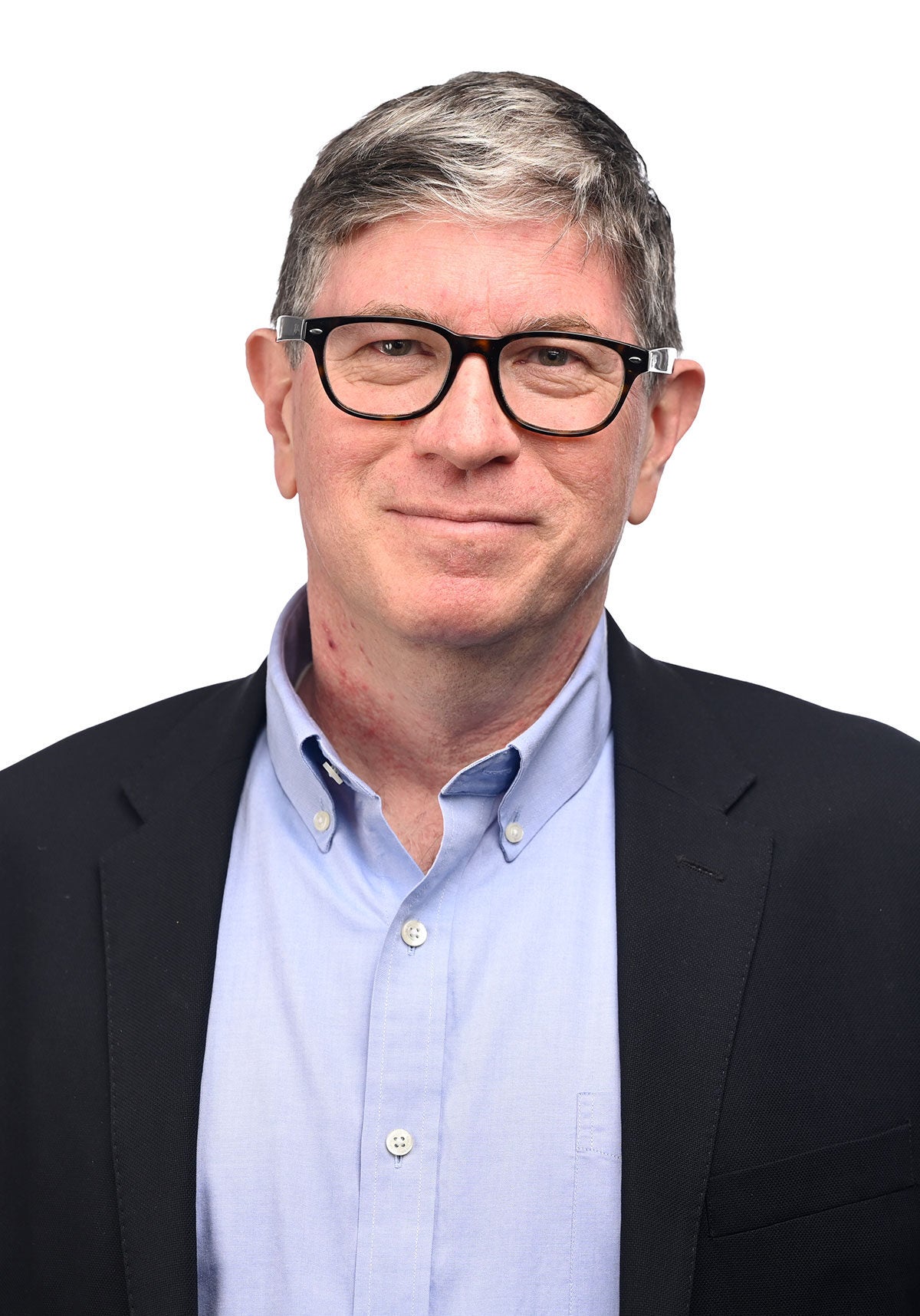 Sean stands facing the viewer in front of a white backdrop, with a serious, slight smile. He's wearing a black suit jacket and light blue collared shirt.