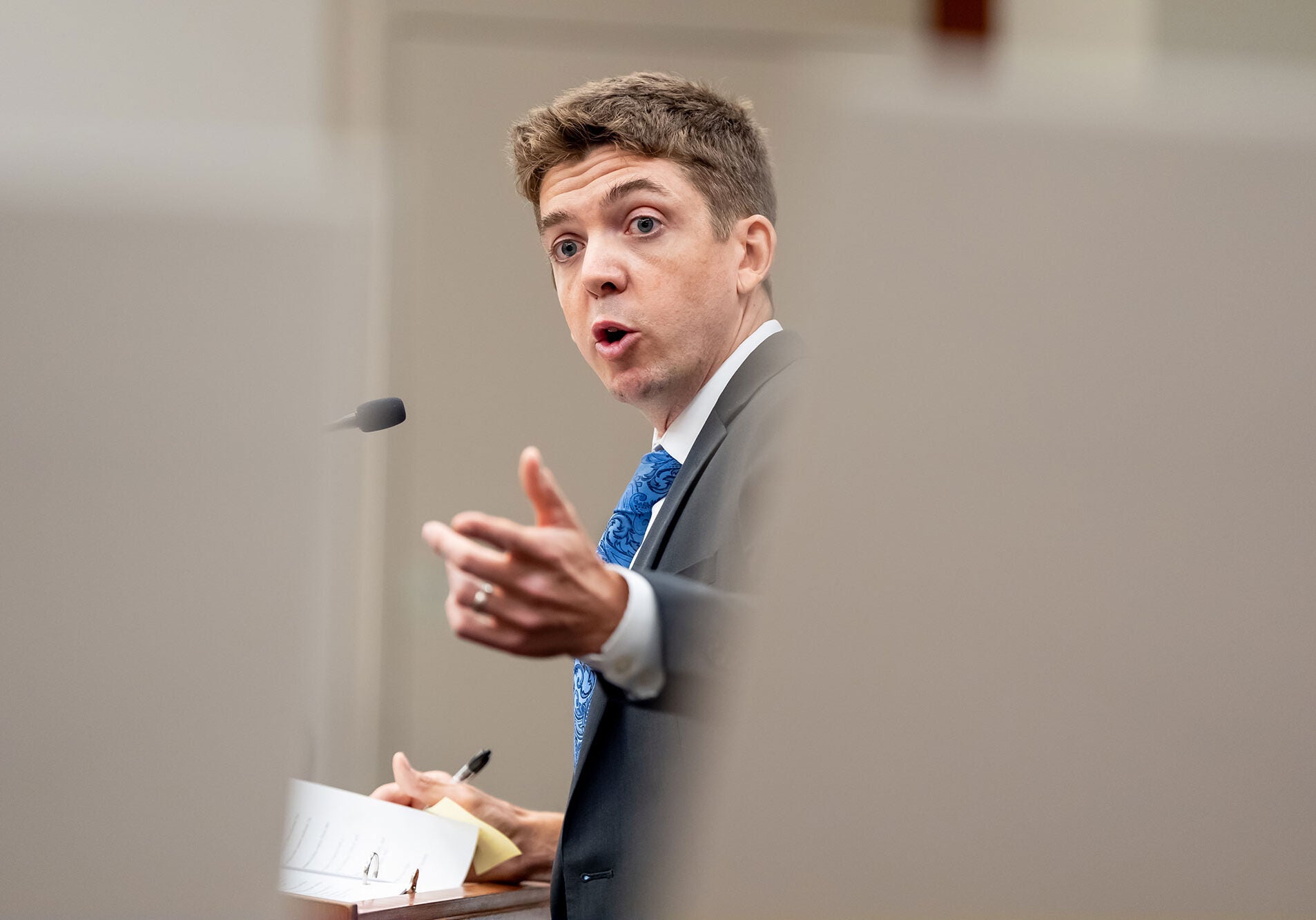 Stu Gillespie, wearing a dark-colored suit, addresses the court with an outstretched hand.