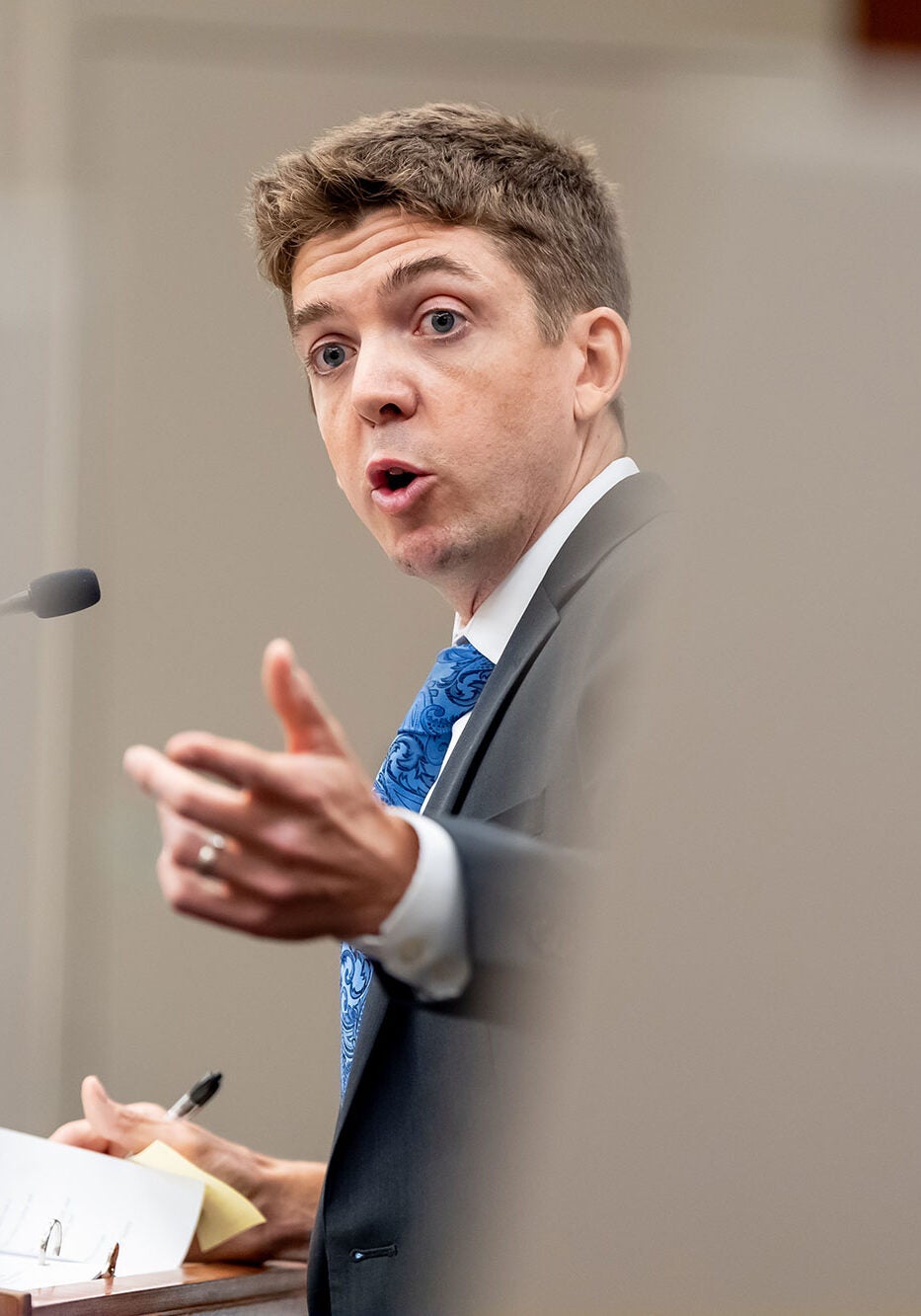 Stu Gillespie, wearing a dark-colored suit, addresses the court with an outstretched hand.