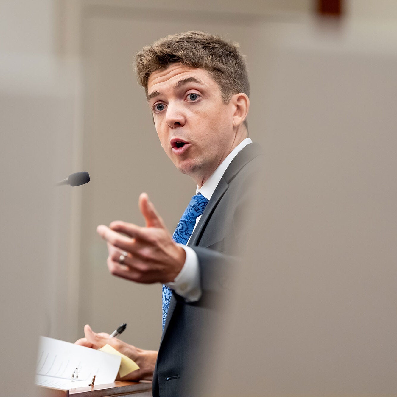 Stu Gillespie, wearing a dark-colored suit, addresses the court with an outstretched hand.