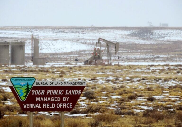 A Bureau of Land Management sign is in the foreground, with an oil derrick behind it.