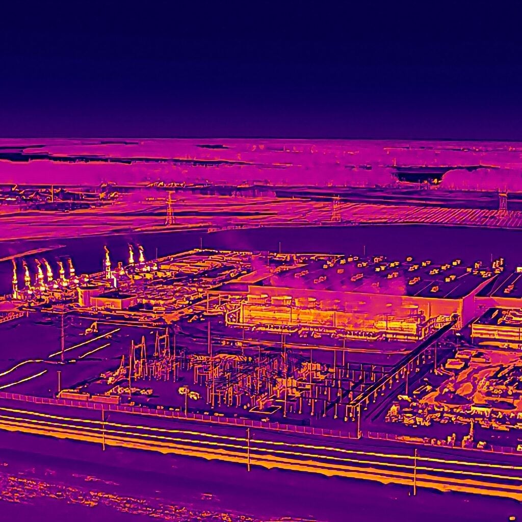 A purple-hued thermal image shows emissions from a row of turbines as bright yellow. The emissions are not visible with the unaided human eye.