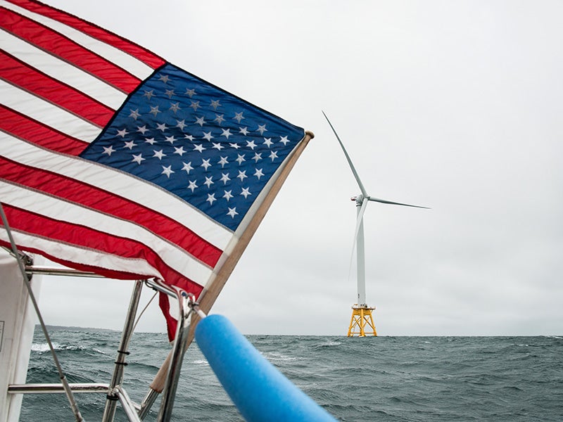 View of a wind turbine off the coast of Block Island, Rhode Island from a boat donned with a waving U.S. flag