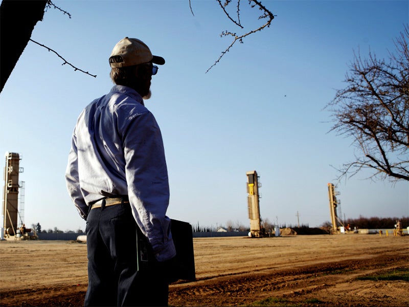 A farmer watches oil wells that have sprouted near almond orchards in Shafter, Kern County, California.