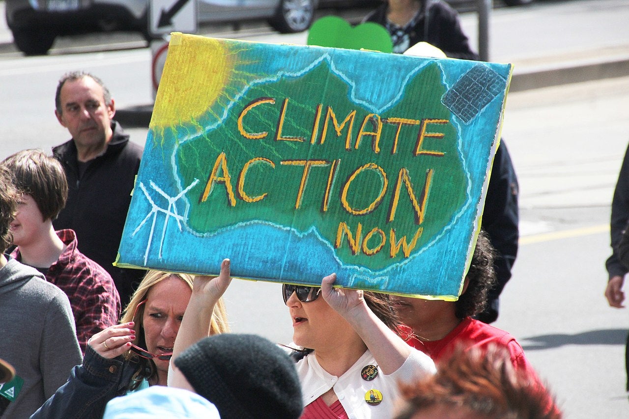 Photo of an Australian woman holding a protest sign reading, "Climate Action Now."