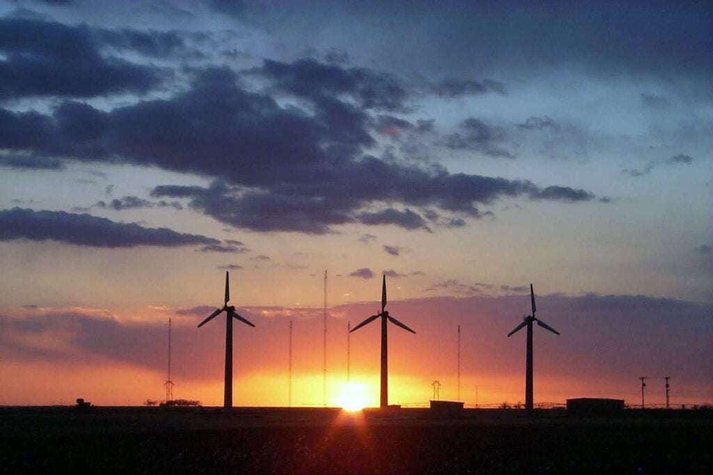 Three wind turbines stand in Bushland, Texas, with the sun setting behind them.