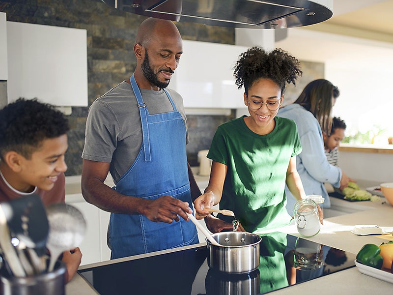 A father cooks with his family on an induction stove. The building electrification movement has been gaining steam as a major climate and clean air solution (Halfpoint Images / Getty Images)