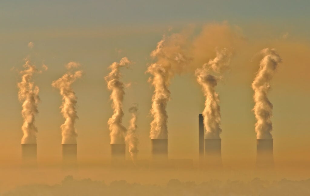 Smokestacks loom up from a hazy sky, tinged with orange, at sunset.