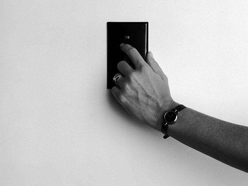A hand turns on a light switch on the wall.