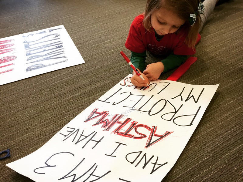 Fiona helps prepare a sign that reads "I am 3 years old and I have asthma. Protect my lungs."