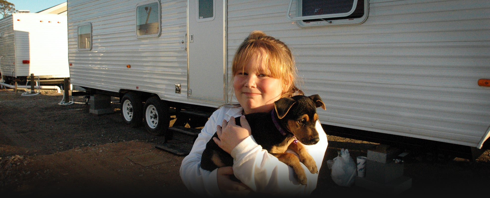Brianna Edson, a Mississippi resident, and her new dog Dixie in front of the travel trailer serving as their temporary home along with Brianna&#039;s mother Wendy (not pictured) at the Ingalls-Wright Emergency Group Site, in November 2005.