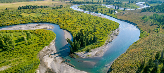 Snake River's blue waters stand out against green landscape with Teton Mountain Range ascending in the background. Grand Tetons National Park, Teton County, Wyoming. (Edwin Remsberg / Getty Images)