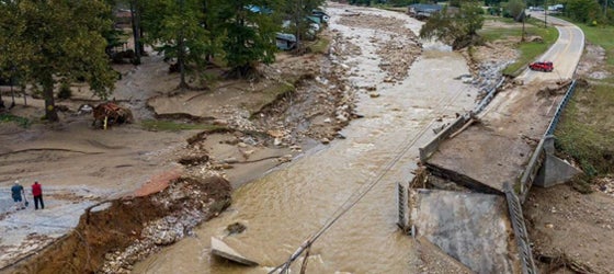 A brown, washed out river with eroded banks with a two-lane bridge in the foreground that has completely collapsed into the water. (Julia Wall for the Washington Post via Getty Images)