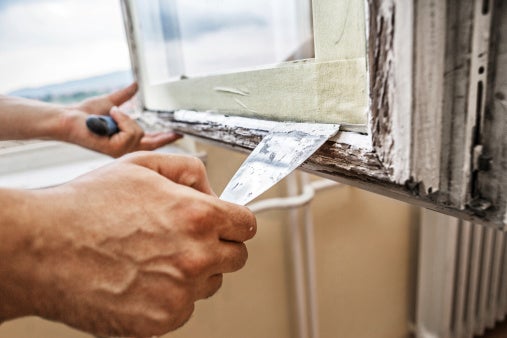 Close-up photo of hands scraping old paint from a window frame.