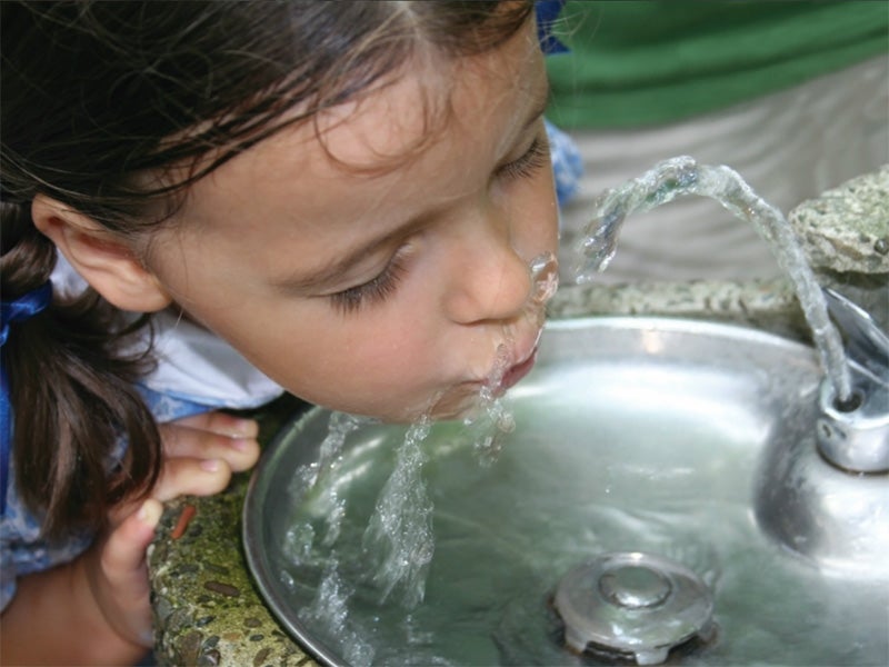 A girl drinks from a water fountain.