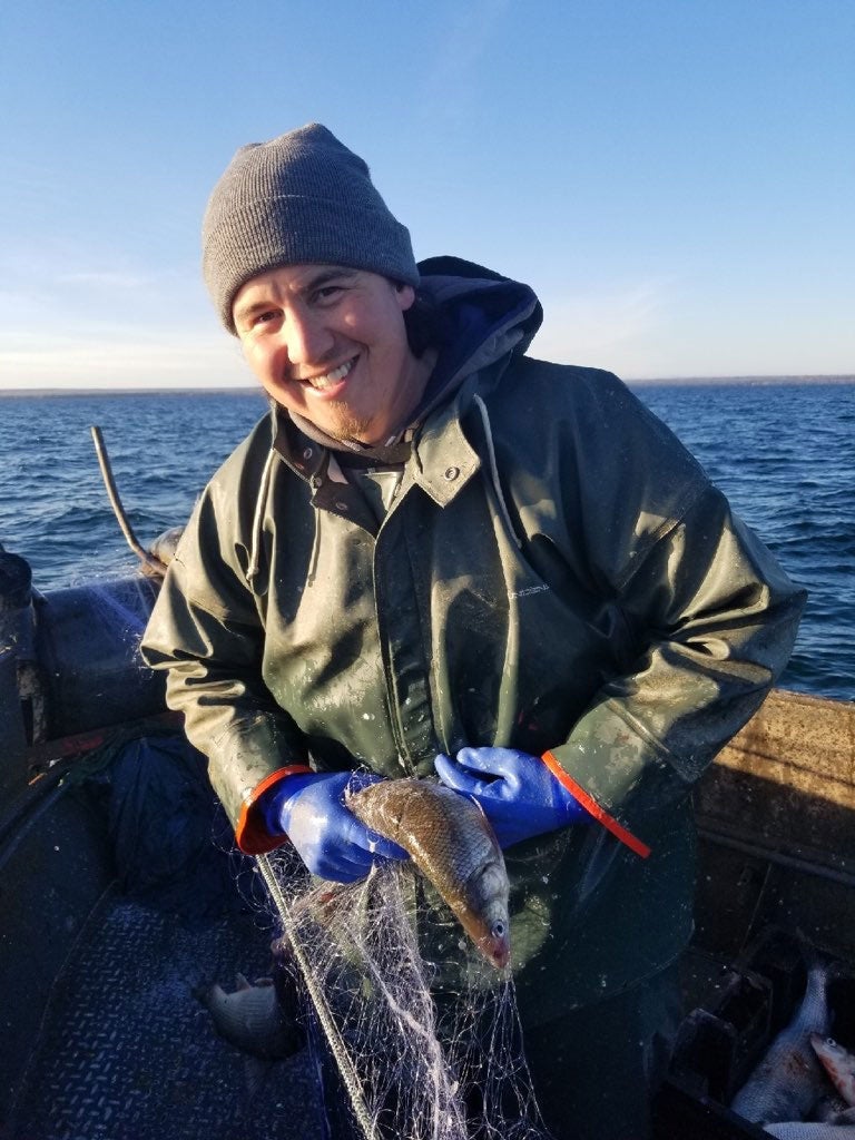 Jacques LeBlanc Jr. holding onto a fish while on a boat, dressed in rain slickers and blue rubber gloves.