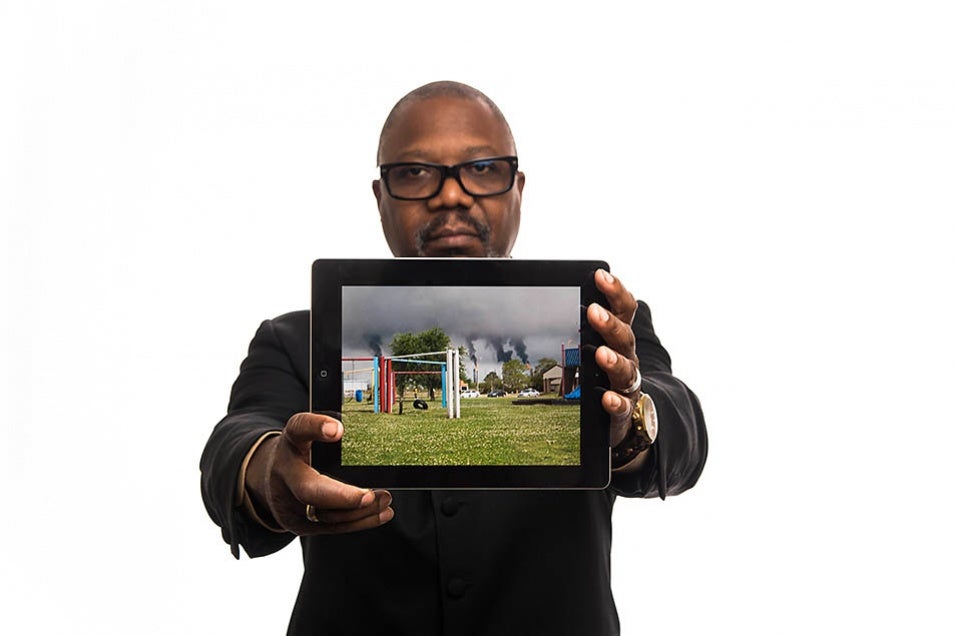 Hilton Kelley holds an image of an oil refinery &quot;flaring&quot; near a community playground in Port Arthur, Texas.