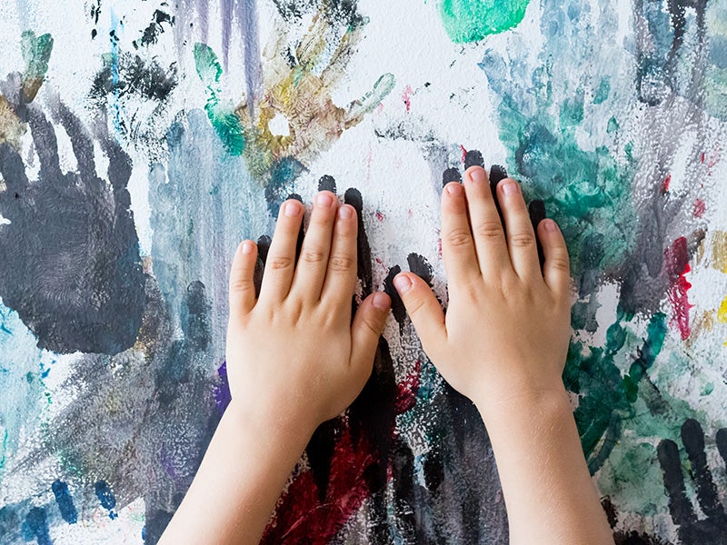 A child paints handprints on the wall.