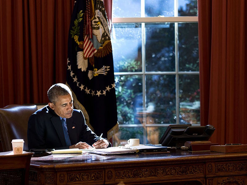 Afternoon autumn light bathes the President as he works at the Resolute Desk in the Oval Office.