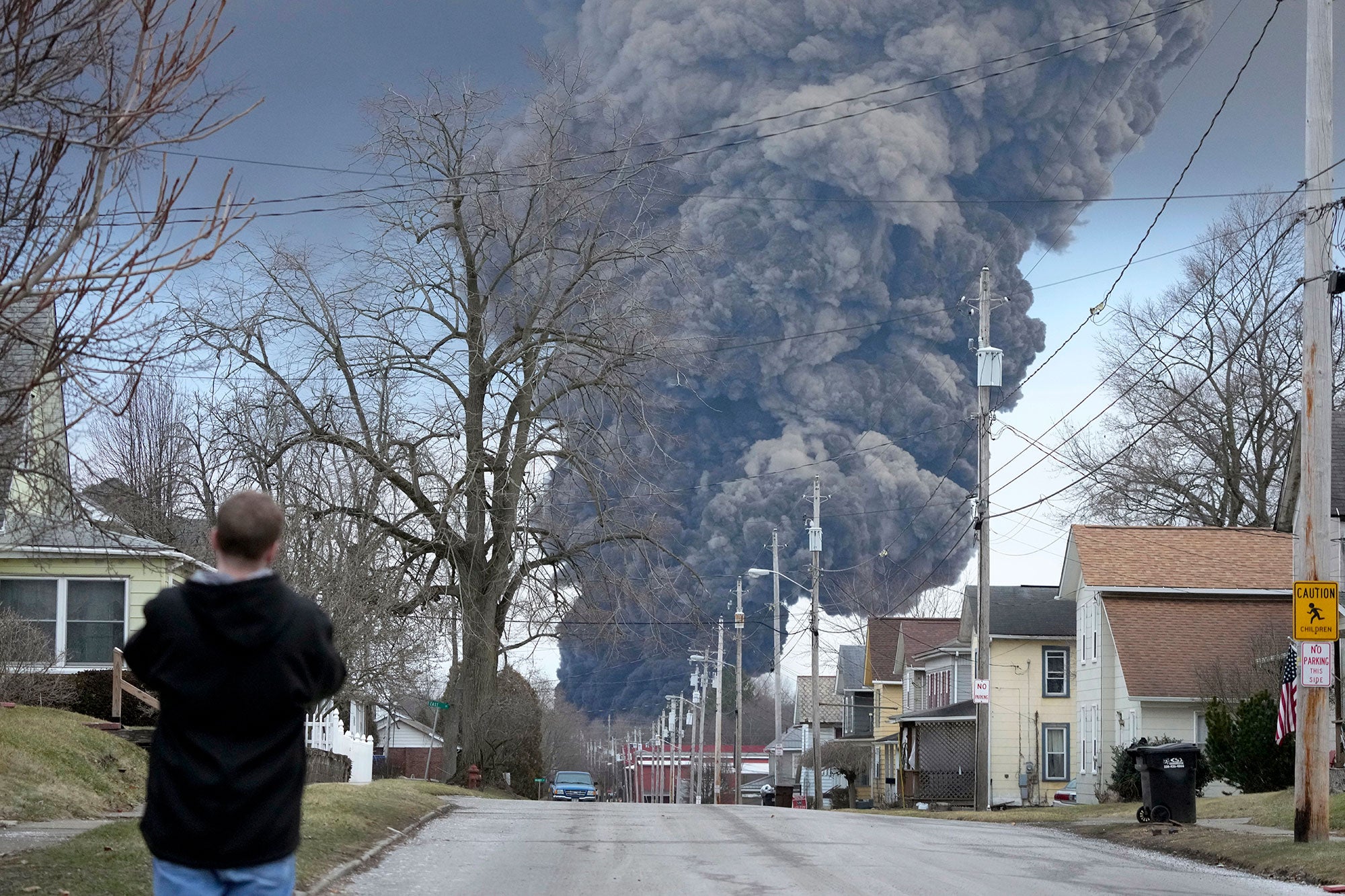 A man takes photos as a black plume rises over East Palestine, Ohio, as a result of a controlled detonation of a portion of the derailed Norfolk Southern train, Feb. 6, 2023. After toxic chemicals were released into the air from a wrecked train in Ohio, evacuated residents remain in the dark about what toxic substances are lingering in their vacated neighborhoods while they await approval to return home.
