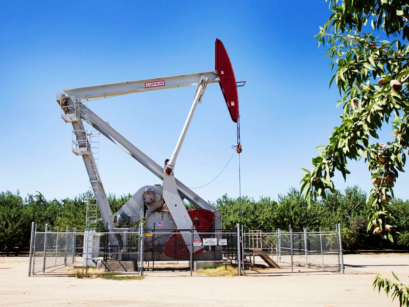 An oil pumpjack towers above almond orchards in Shafter, CA, a small city in Kern County.