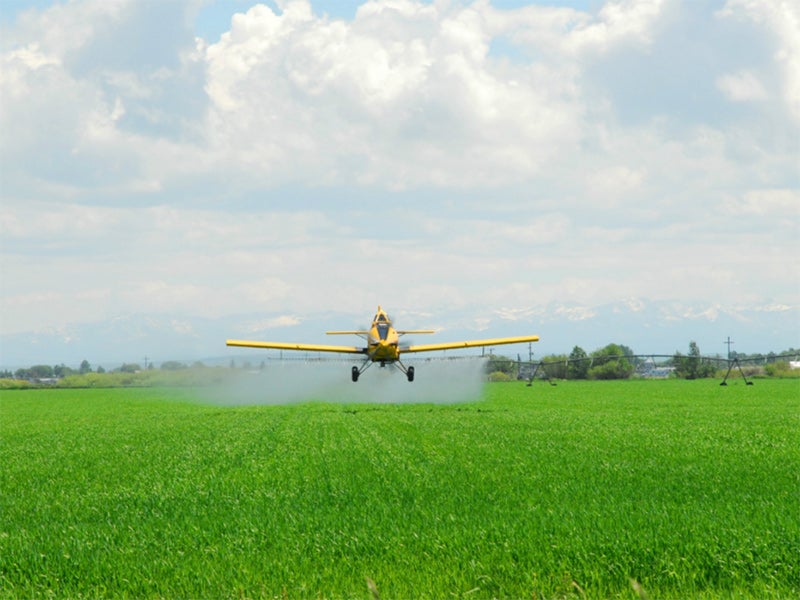 A crop duster sprays pesticides over a farmfield.
(Denton Rumsey / Shutterstock)