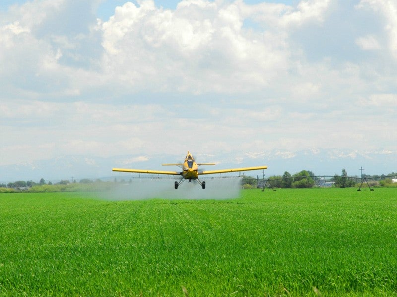 A crop duster sprays pesticides over a farmfield.
(Denton Rumsey/Shutterstock)