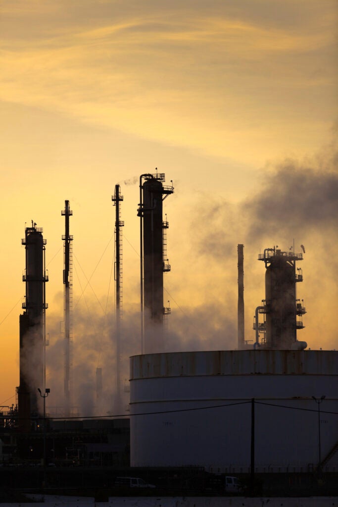 Smoke stacks and distillation towers at a large petrochemical plant are silhouetted against the golden evening sky.
(iStock)