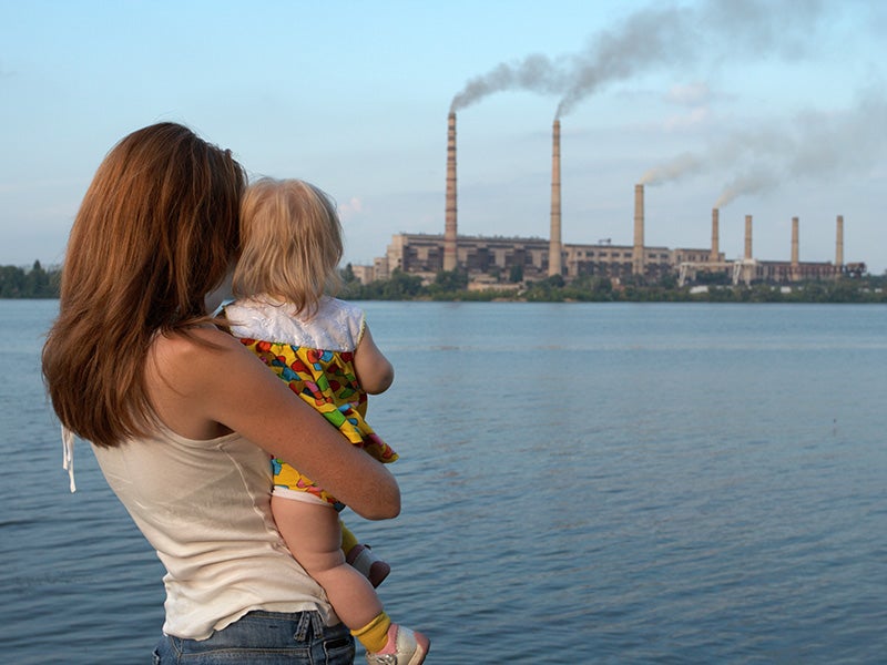 A woman and child watch a power plant across a lake.