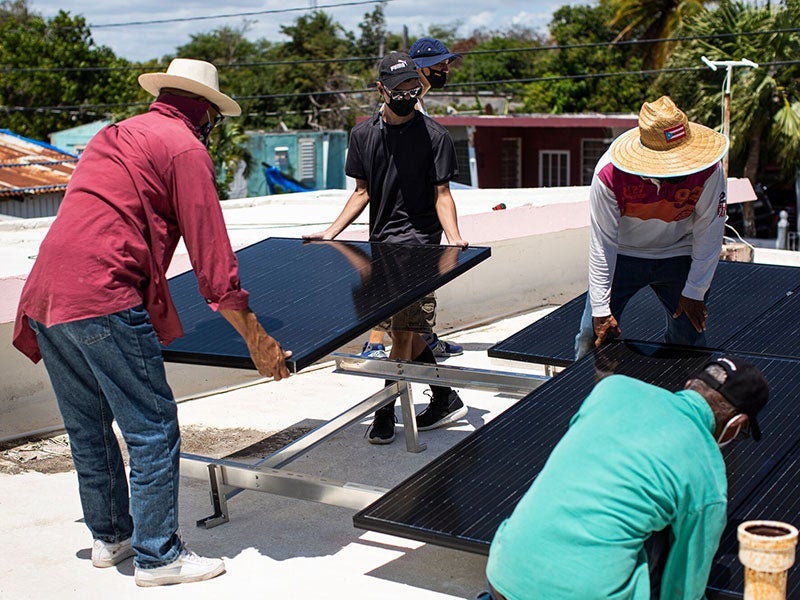 Volunteers with the group Comunidad Guayamesa Unidos por tu Salud help install a solar power system on a community elder's home at Puente de Jobos in Guayama, P.R., on Mar. 20, 2021. The initiative by the group Comunidad Guayamesa Unidos por tu Salud (Guayama’s Community United for Your Health) has installed more than 10 solar powered systems in the area. (Erika P. Rodriguez for Earthjustice)