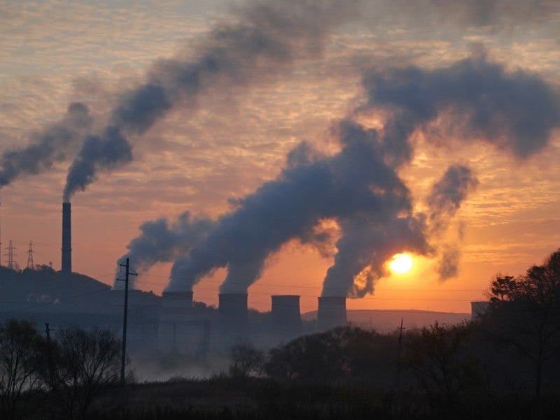 Smoke billows from a series of smokestacks, obscuring the sun.