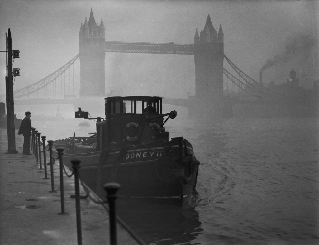 A tugboat on the Thames near Tower Bridge in heavy smog, London, England, 1952.